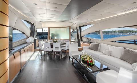 Luxurious motor yacht interior with white seating and dining table, large windows overlooking the sea