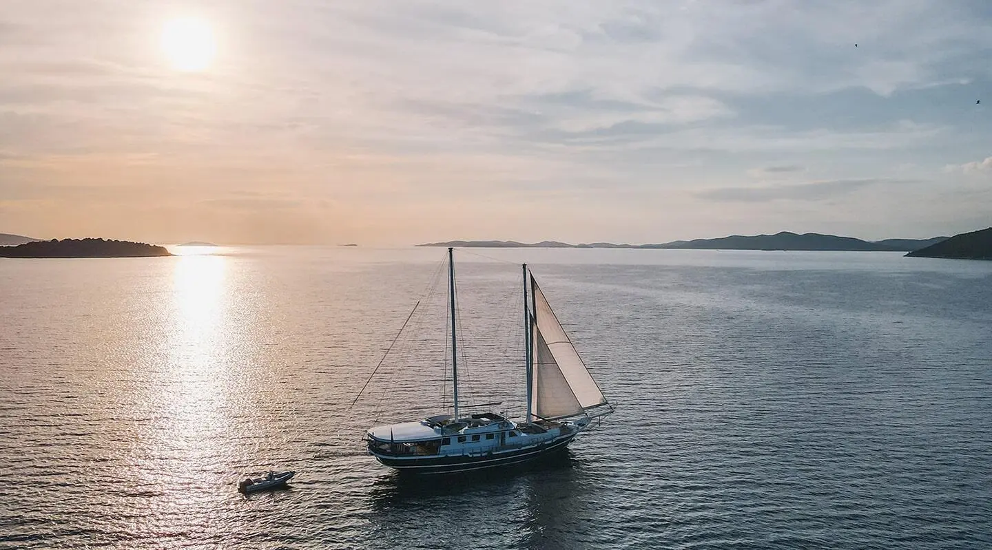 A small sailing yacht named Aurum anchored on calm sunset waters