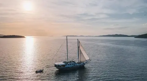 A small sailing yacht named Aurum anchored on calm sunset waters