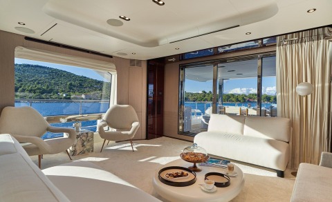 Luxurious Aluminia Too yacht interior: cream sofas, round coffee table with snacks, large windows overlooking blue sea