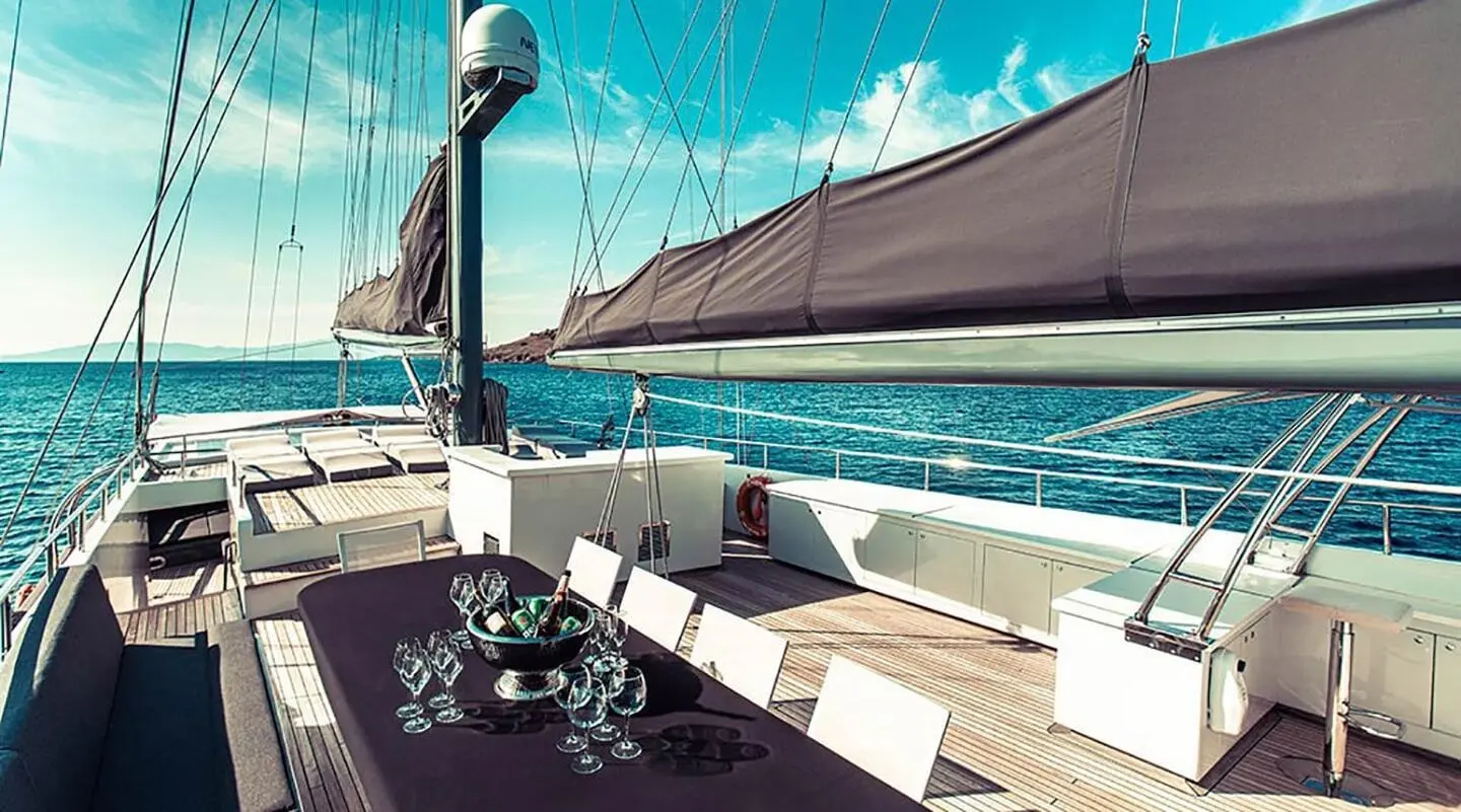 Wide deck with a table and chairs, champagne glasses on the table aboard a sailing yacht
