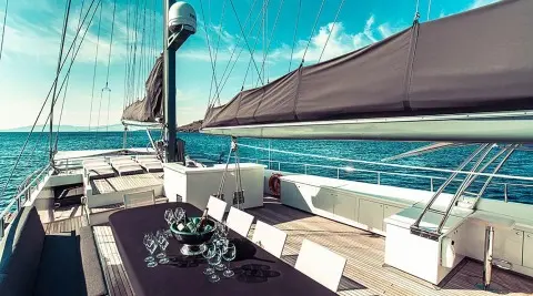 Wide deck with a table and chairs, champagne glasses on the table aboard a sailing yacht