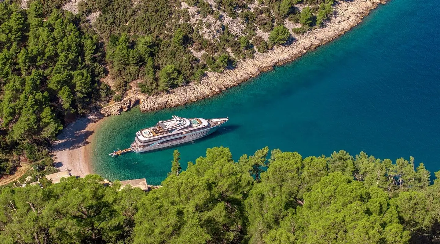 Yacht Freedom anchored near rocky coastline, turquoise water, lush green trees