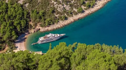 Yacht Freedom anchored near rocky coastline, turquoise water, lush green trees
