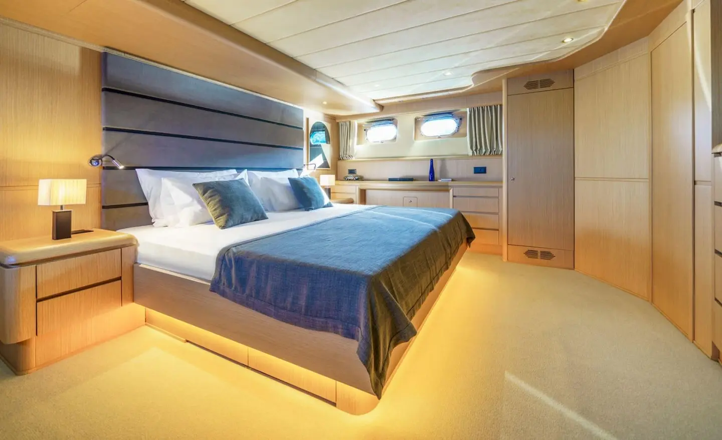 Phantom yacht bedroom with a large bed, blue throw, wooden accents, and warm lighting