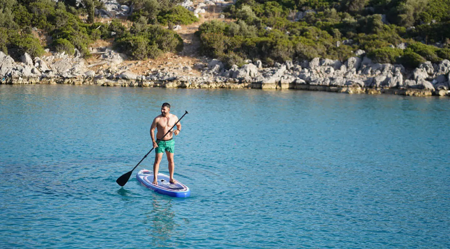 Man on a paddleboard in clear blue water near rocky shoreline