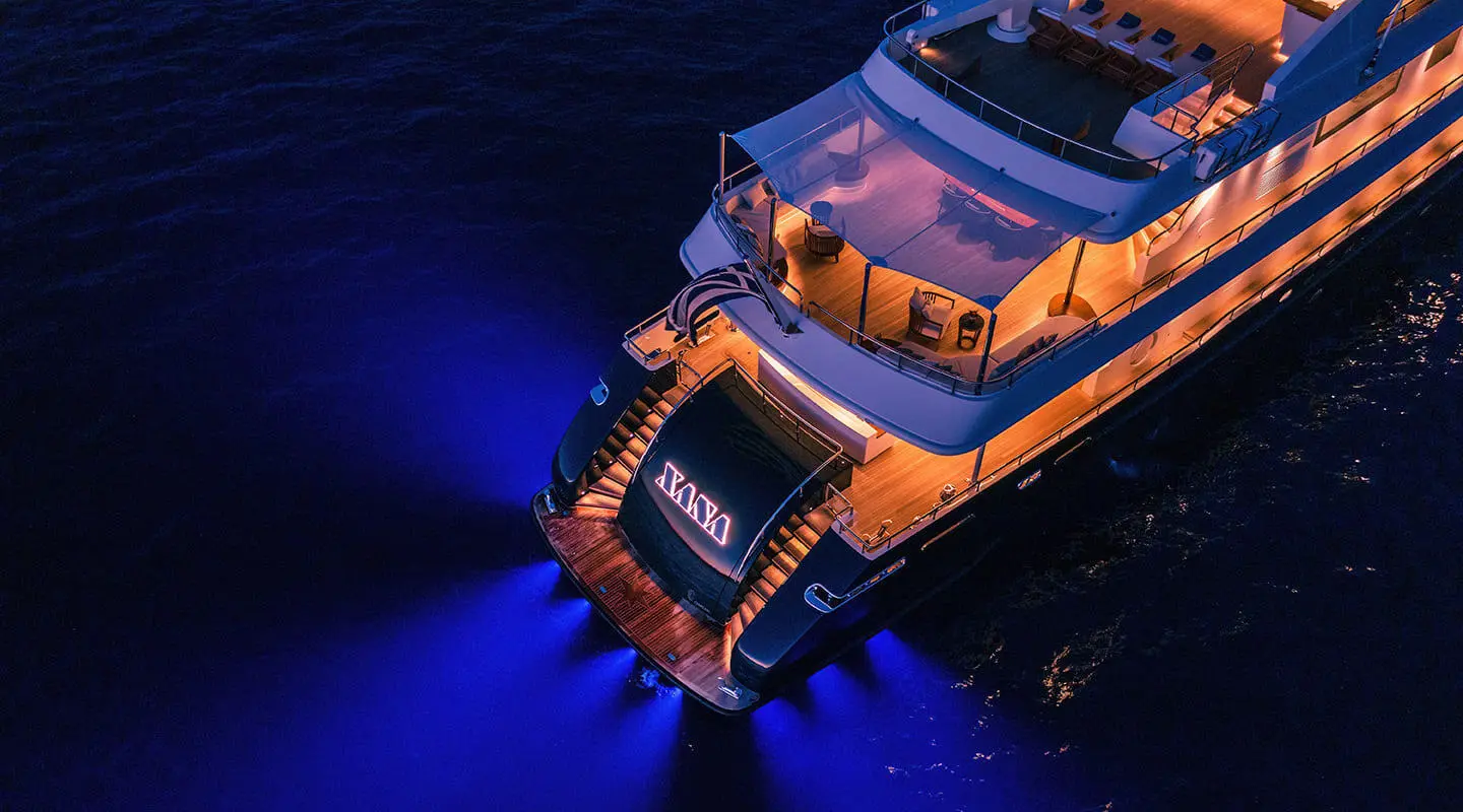 Overhead view of Xana luxury yacht at night, blue water surrounding, warm deck lights