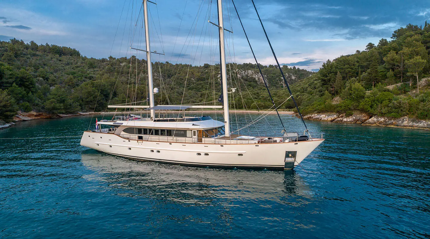 Navilux yacht anchored in calm blue water with a forested shoreline in the background