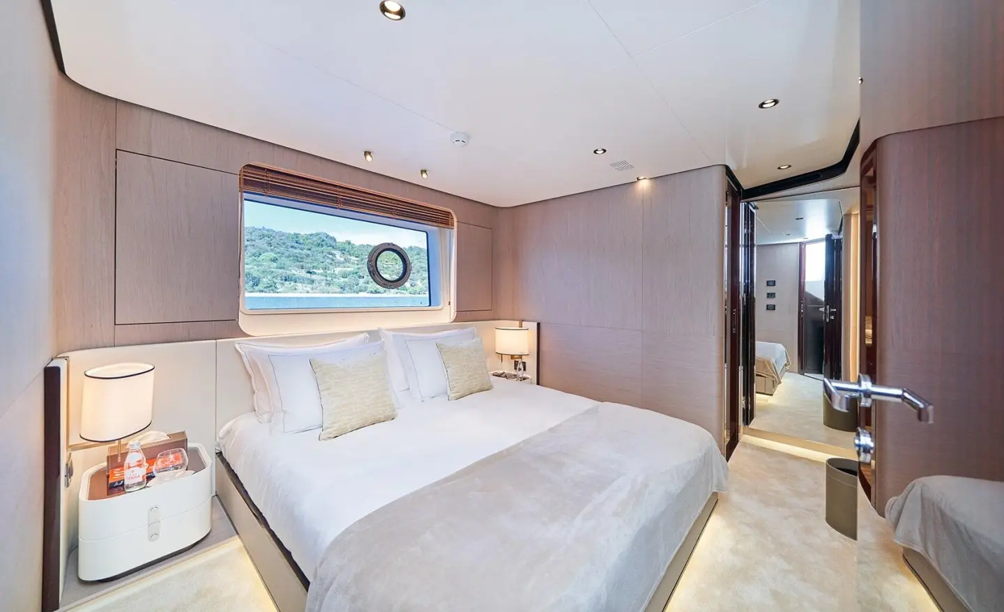 Luxurious yacht bedroom with large window view, white bedding, and wood-paneled walls