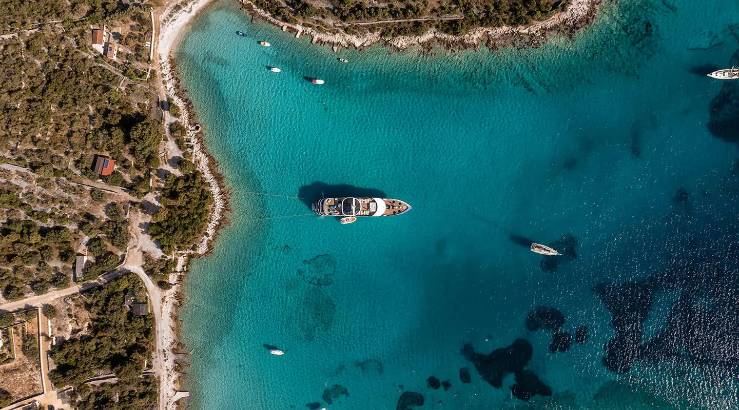 Aerial view of Karizma yacht anchored in clear blue desert shoreline waters at sunset