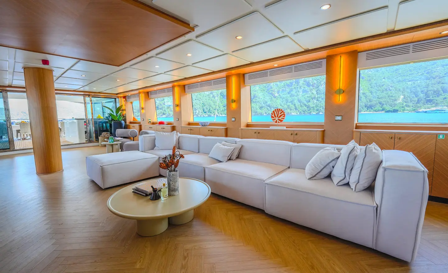 Spacious yacht saloon with large windows, white seating, and round coffee table