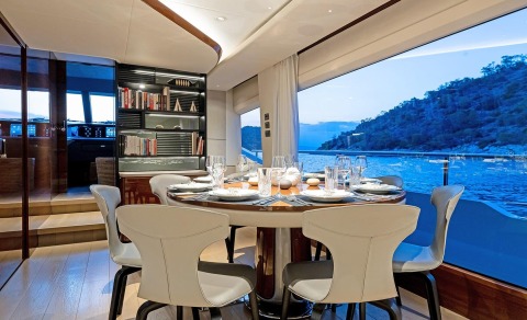 Vista motor yacht saloon with dining table and seating, overlooking sea and coastline