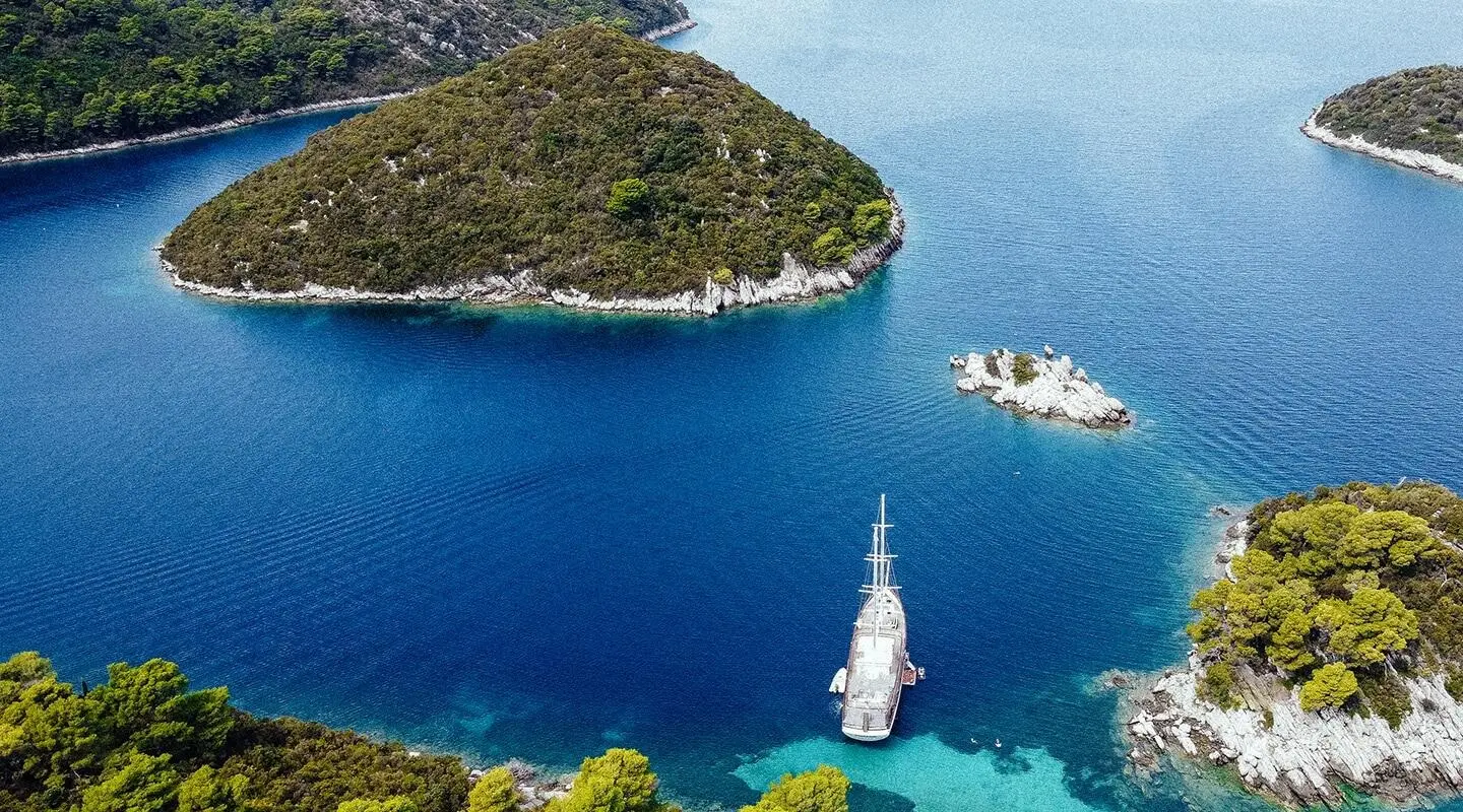 Corsario yacht anchored in a turquoise cove among lush green islands with clear blue water