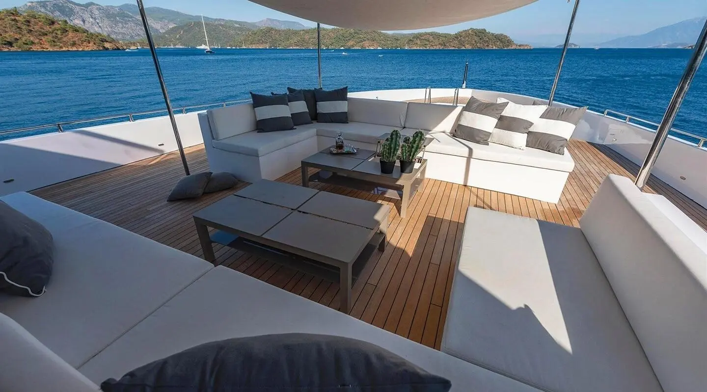 Ocean Breeze yacht deck with sun loungers, shaded seating, and railing overlooking blue sea
