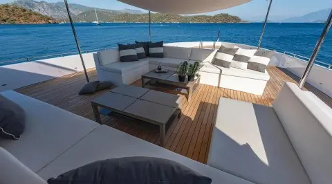 Ocean Breeze yacht deck with sun loungers, shaded seating, and railing overlooking blue sea
