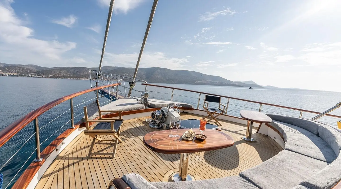 Gozdem The One yacht deck with wooden seating, table, and ocean view at sunset
