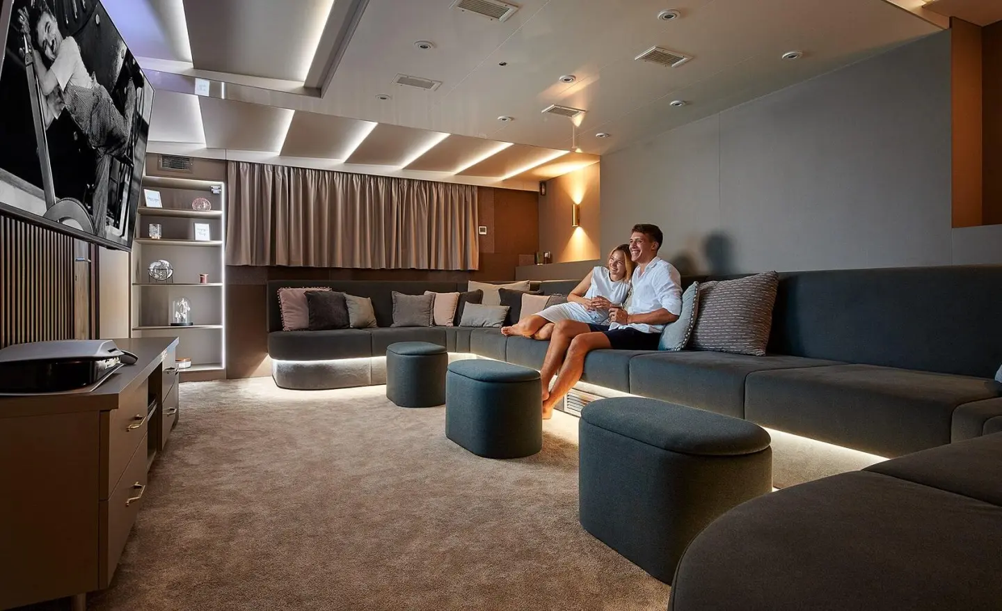 Lupus Mare yacht interior with two people sitting on a long sofa watching TV