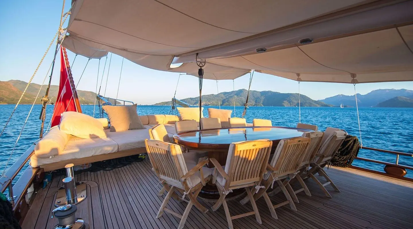 Under A deck canopy, a wooden outdoor seating area aboard a yacht with a view of the sea and distant coastline