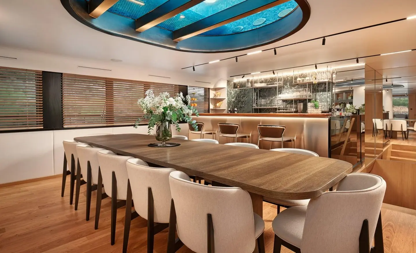 Anetta luxury yacht dining area with long wooden table, white chairs, and overhead blue-tinted windows