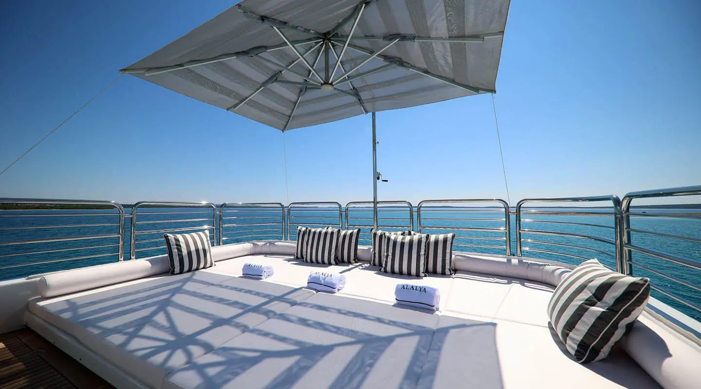 Sunlit yacht deck with lounge chairs and striped cushions under an umbrella