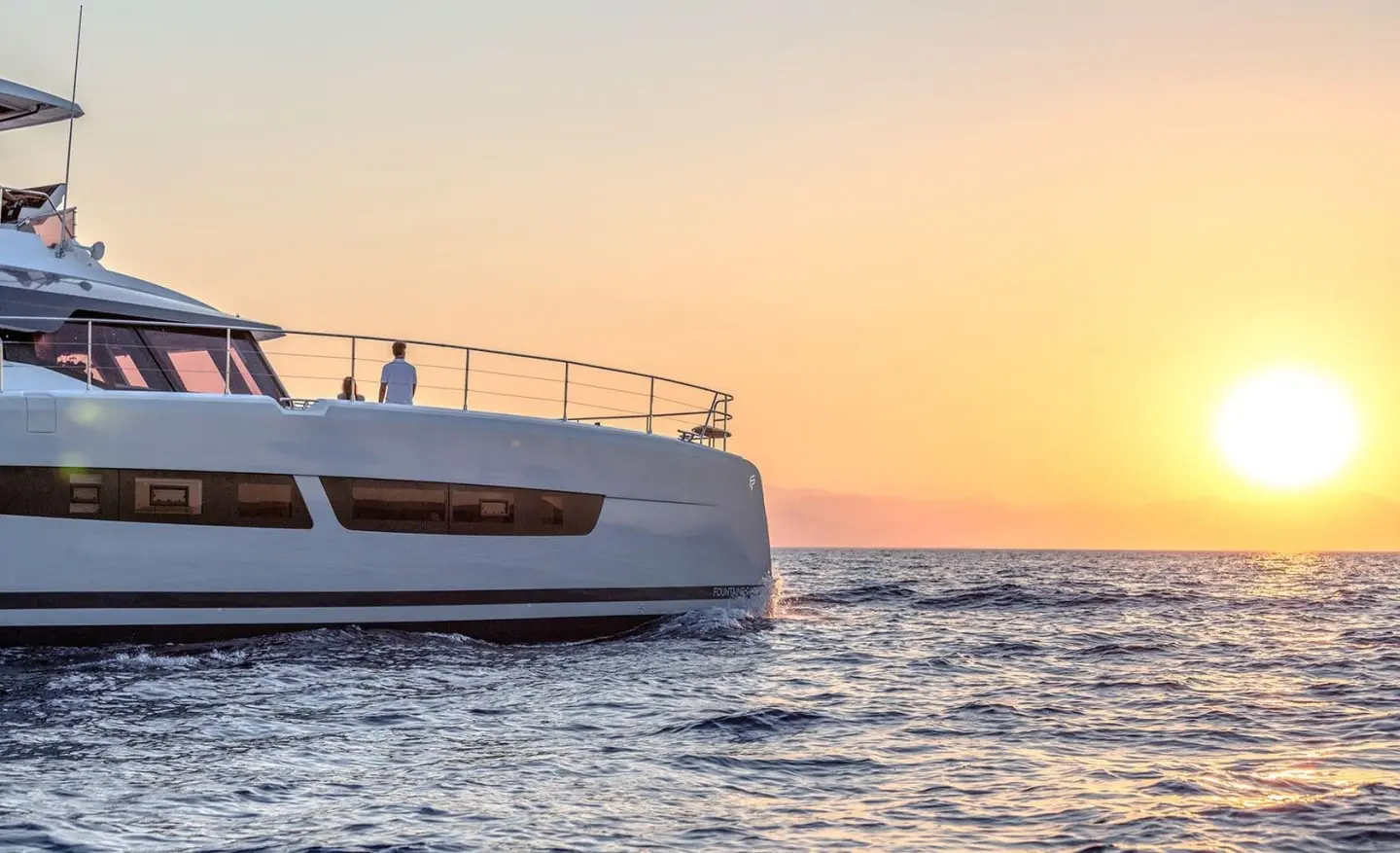 Yacht D2 partially visible at sunset, bow on calm sea with orange sky