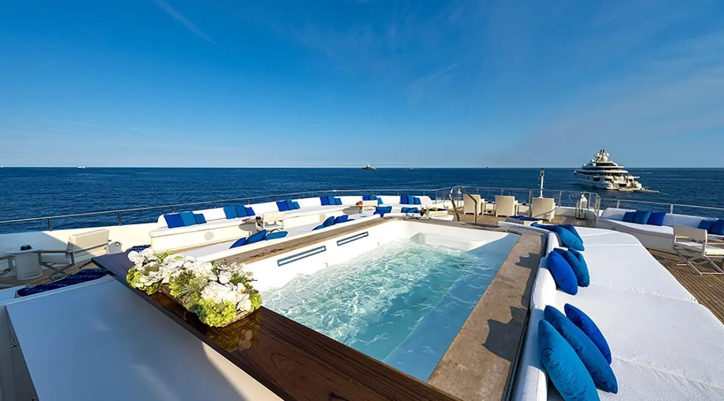 View from a yacht deck with a long pool, white lounge chairs, and clear blue sea