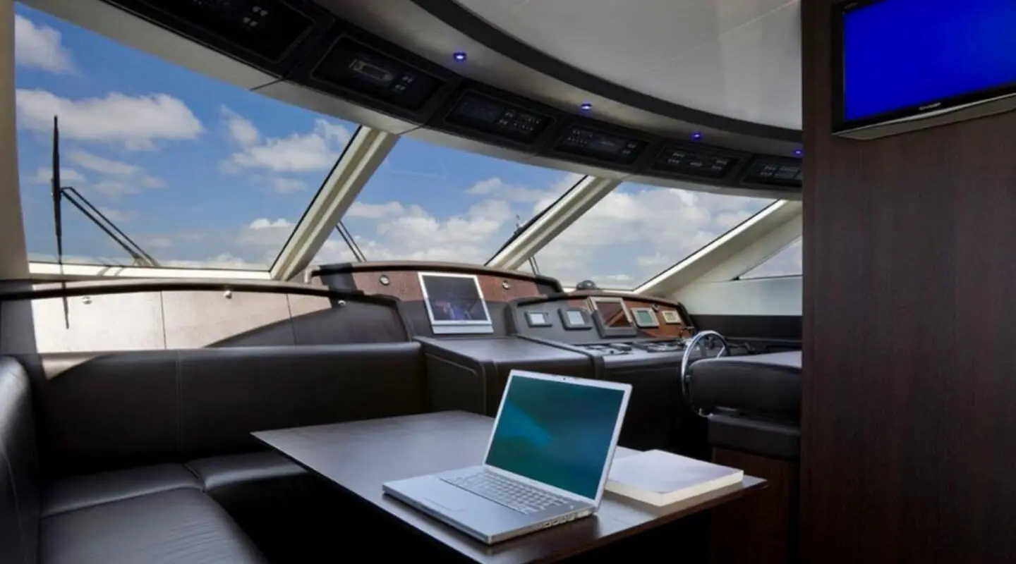 Interior yacht salon with large windows, wooden dashboard, laptop on table