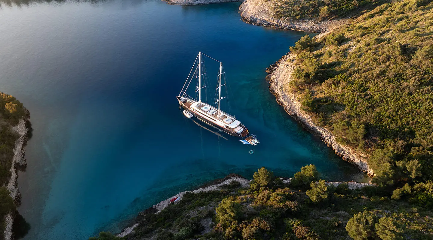 A white sailing yacht anchored near rocky coastline with deep blue water