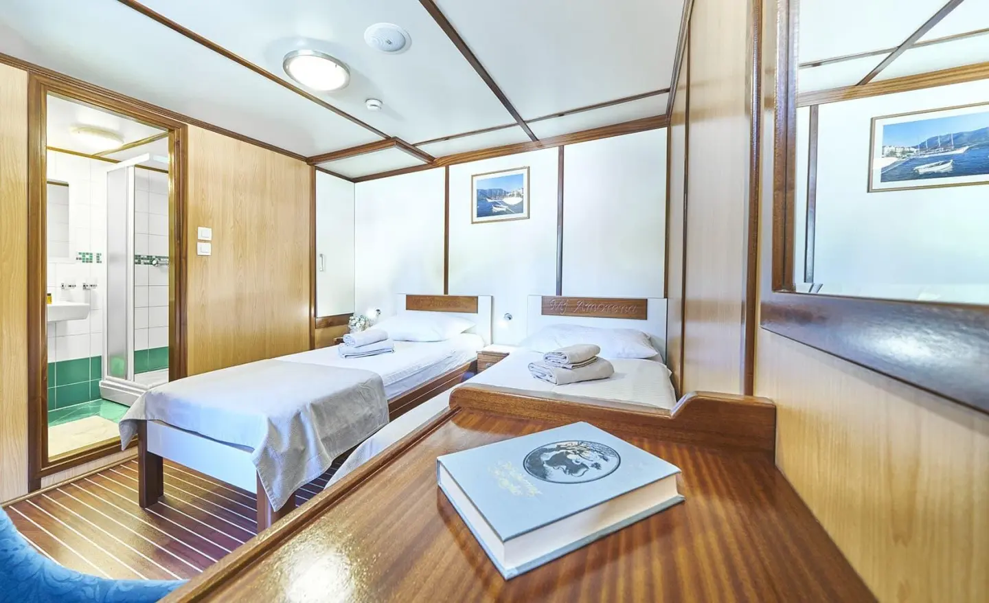 Amorena yacht interior with two beds, wooden deck, windows, and seating area