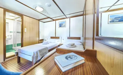 Amorena yacht interior with two beds, wooden deck, windows, and seating area