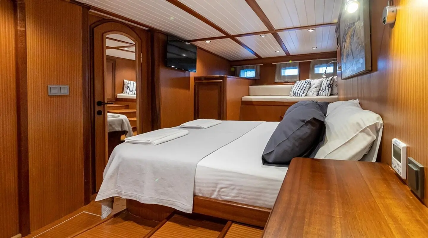 Two neatly made beds in a wood-paneled yacht cabin with a window view