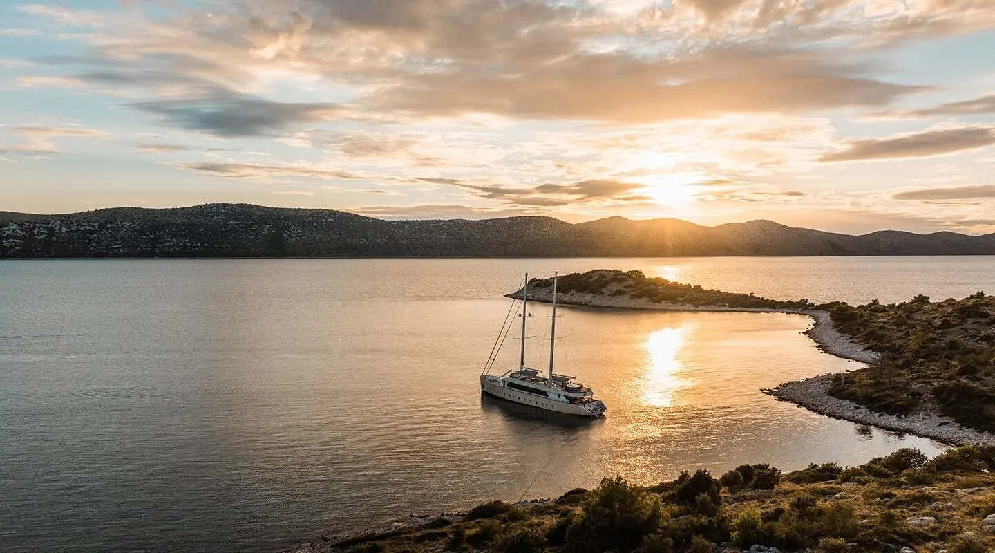 Sunset over calm water with a small motor yacht anchored near rocky shore