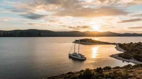 Sunset over calm water with a small motor yacht anchored near rocky shore
