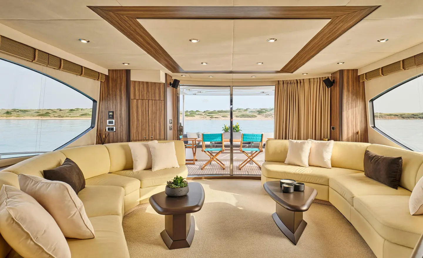 Luxurious yacht saloon with cream sofas and a wooden table, view to the deck.