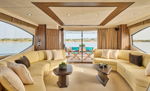 Spacious lounge aboard a luxury yacht with cream seating and wooden panel walls, open rear doors to an outdoor deck