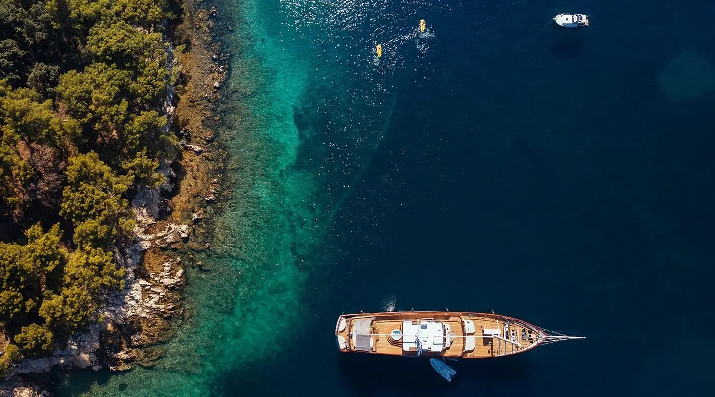 Overhead view of a sleek yacht anchored near turquoise sea and rocky coastline