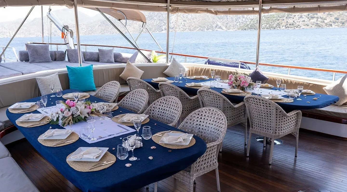 Nevra Queen yacht dining area on deck with blue tablecloths and wicker chairs at sunset