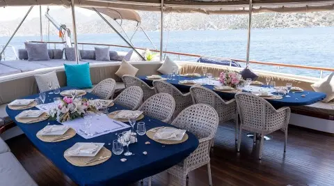 Nevra Queen yacht dining area on deck with blue tablecloths and wicker chairs at sunset