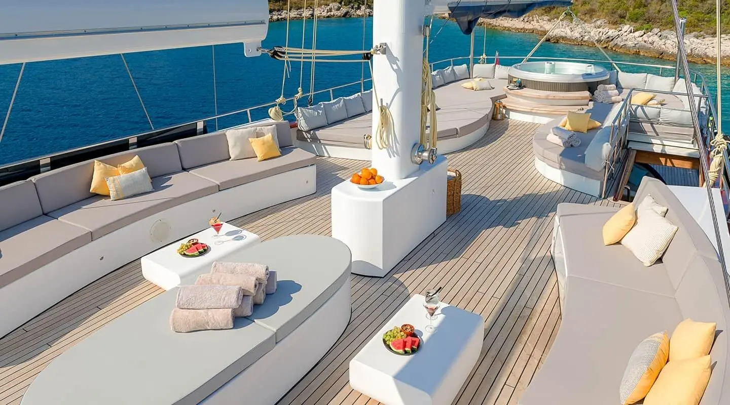 Sunlit upper deck lounge with beige cushions and yellow pillows on a yacht