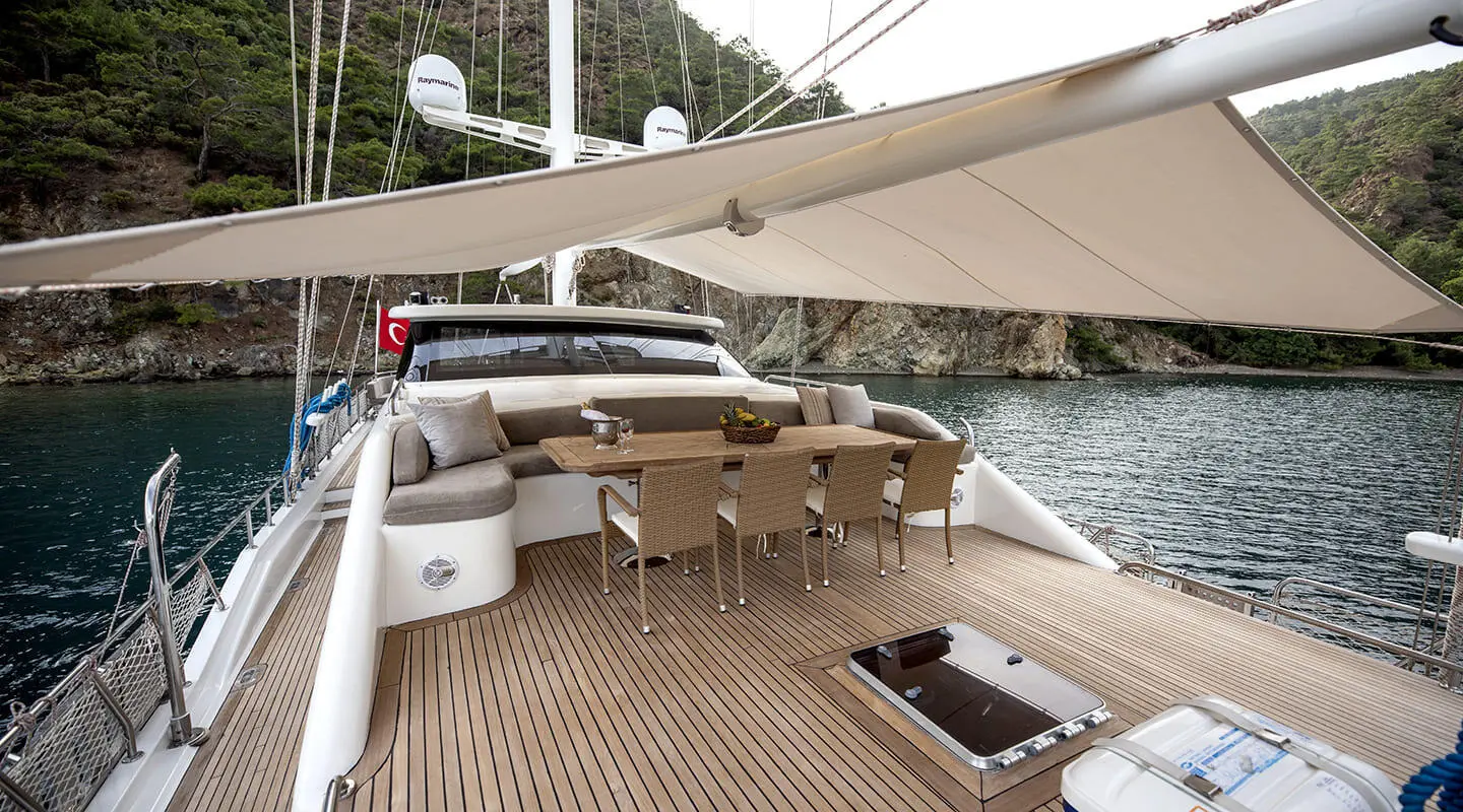 Kayhan 3 yacht deck with wooden seating, shaded awning, and view past railing at sunset