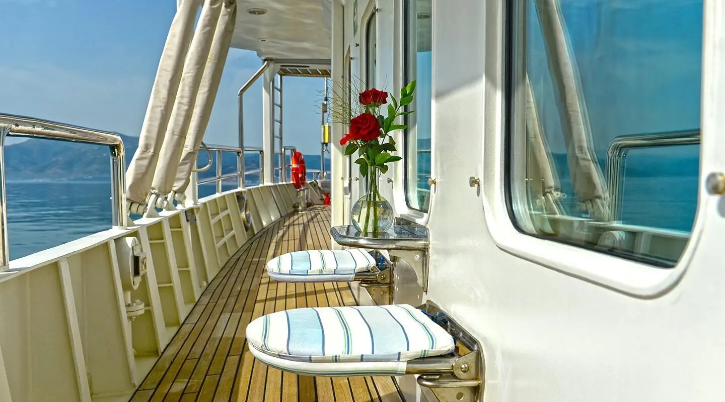 Gulet yacht deck with sun loungers, cushions, and potted flowers along a wooden railing