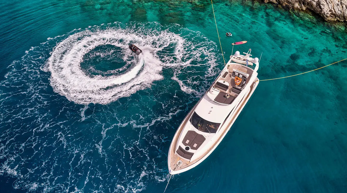 Small motor yacht named M Five cruising turquoise water near a rocky coastline