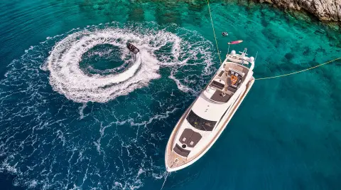 Small motor yacht named M Five cruising turquoise water near a rocky coastline