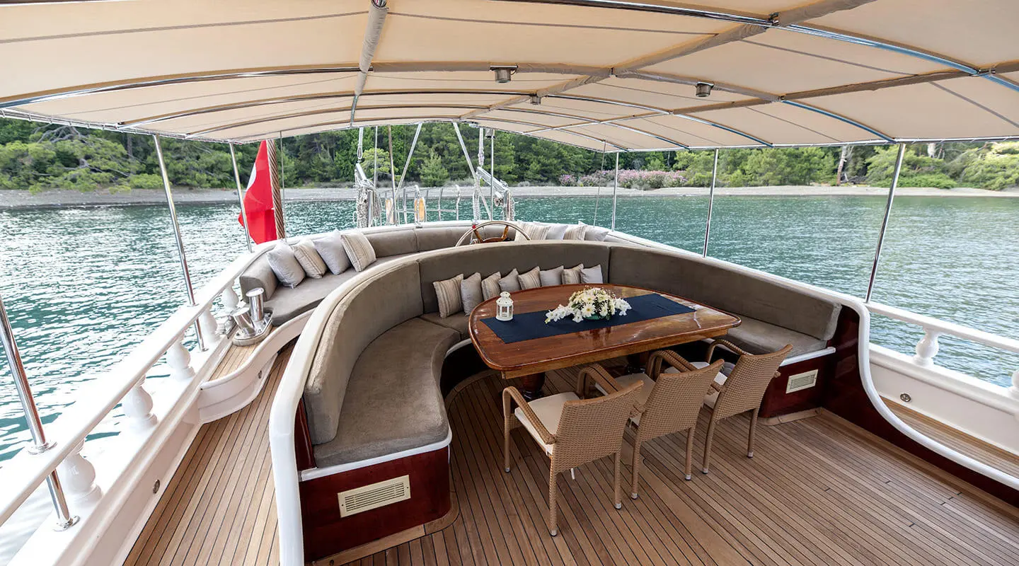 Yacht Kayhan 5 aft deck with wicker seating and dining table under canopy at sunset
