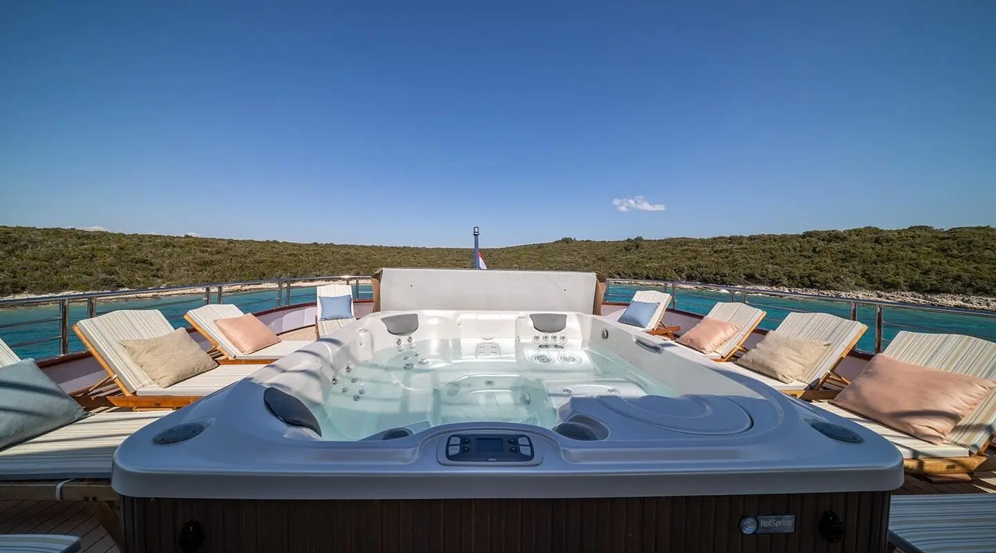 Olimp luxury yacht deck with a hot tub and multiple lounge chairs in sunlit harbor