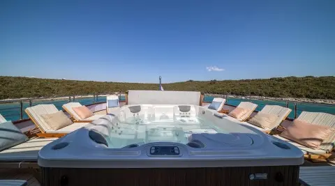 Olimp luxury yacht deck with a hot tub and multiple lounge chairs in sunlit harbor