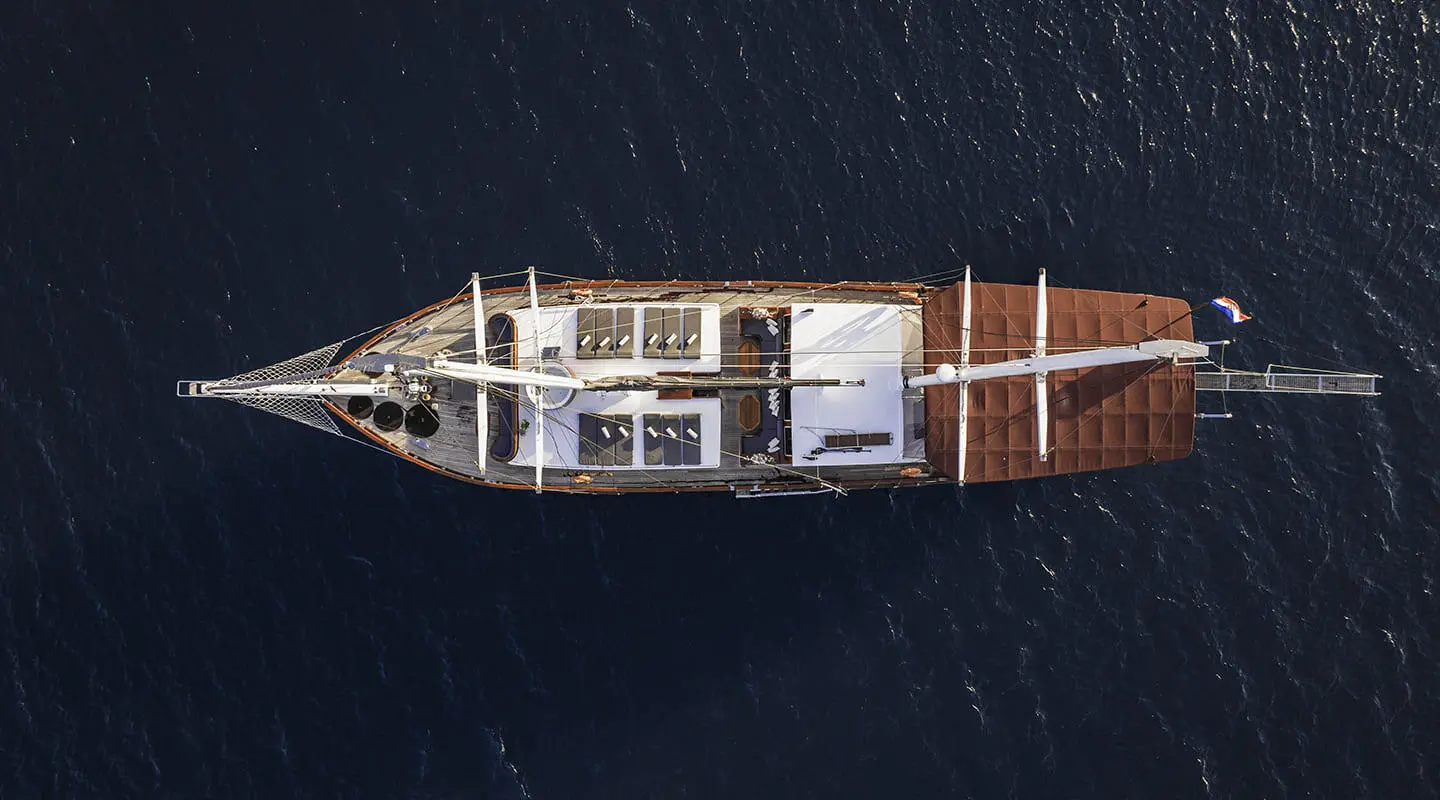 Top-down view of a sleek yacht with white deck and dark hull sailing on calm blue water at sunset