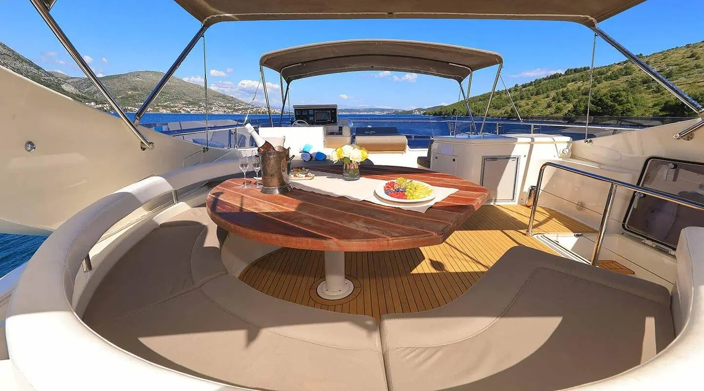 Quo Vadis I yacht deck with wooden table, seating, and sunshade on blue water