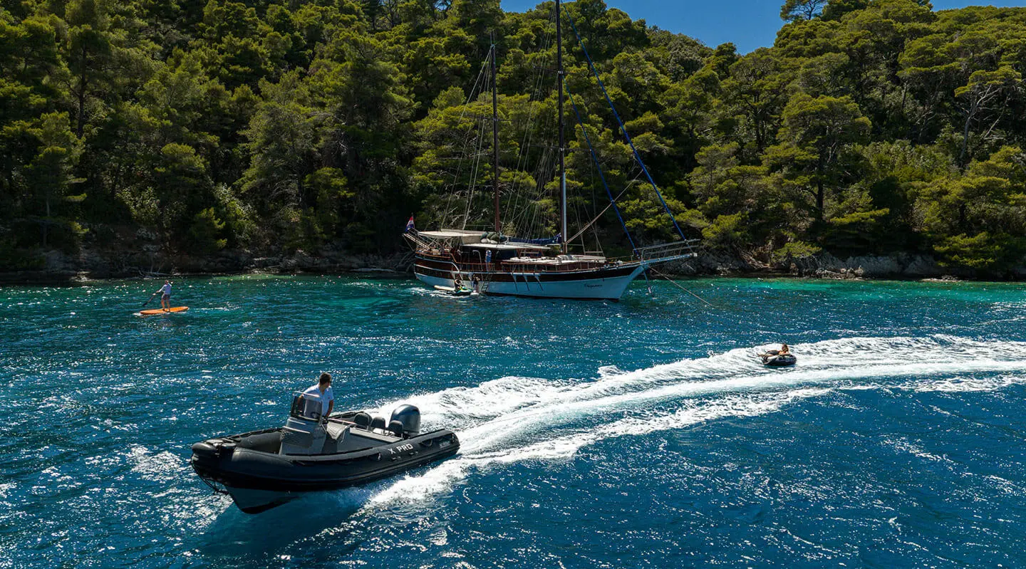 Eleganza yacht anchored near rocky coastline with clear blue water and small boat nearby