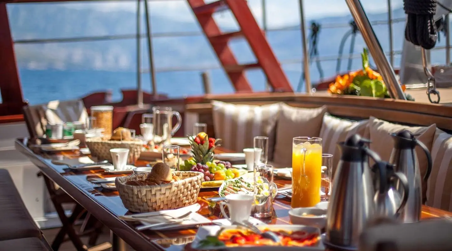Romanca luxury gulet yacht dining setup at sunset with plates and drinks